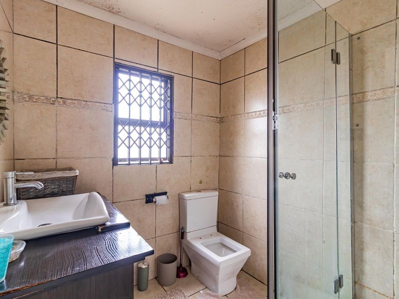 A compact bathroom featuring a glass-enclosed shower, vessel sink vanity, and tiled walls, requiring attention to ceiling maintenance.