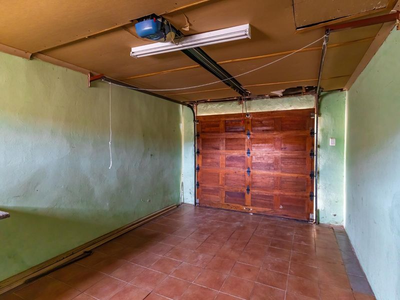 A spacious, empty garage featuring tiled flooring, a wooden sectional door, and exposed ceiling infrastructure, offering potential for storage or workshop conversion.