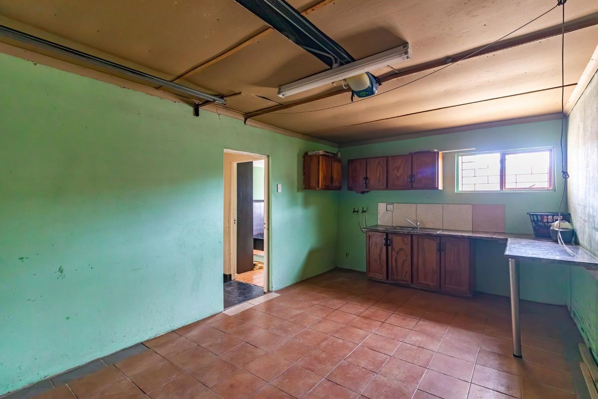 A functional kitchen space featuring built-in wooden cabinetry, tiled flooring, and a tiled splashback, currently in need of cosmetic updates and ceiling repairs.