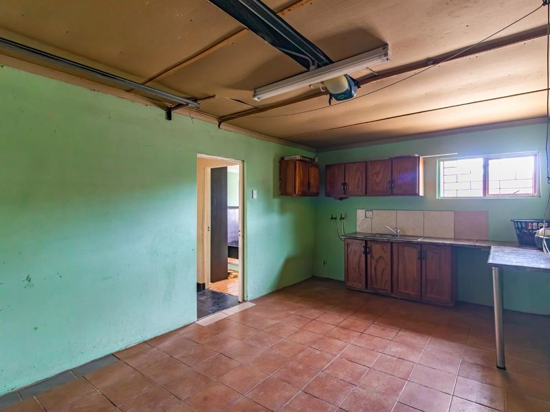 A functional kitchen space featuring built-in wooden cabinetry, tiled flooring, and a tiled splashback, currently in need of cosmetic updates and ceiling repairs.
