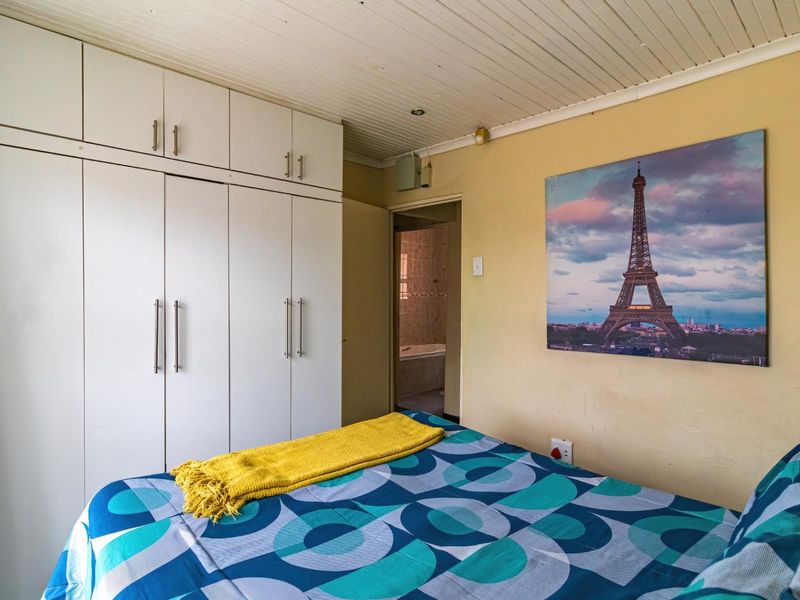 A bedroom featuring built-in cupboards and timber-look ceiling panels, with an adjoining bathroom visible through the doorway.
