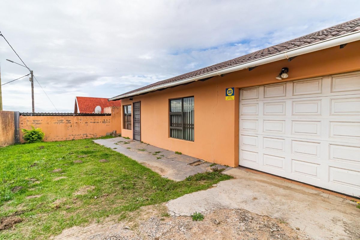 Rear exterior view of the property featuring a single garage, concrete apron, and a surrounding boundary wall with a grassed yard area.