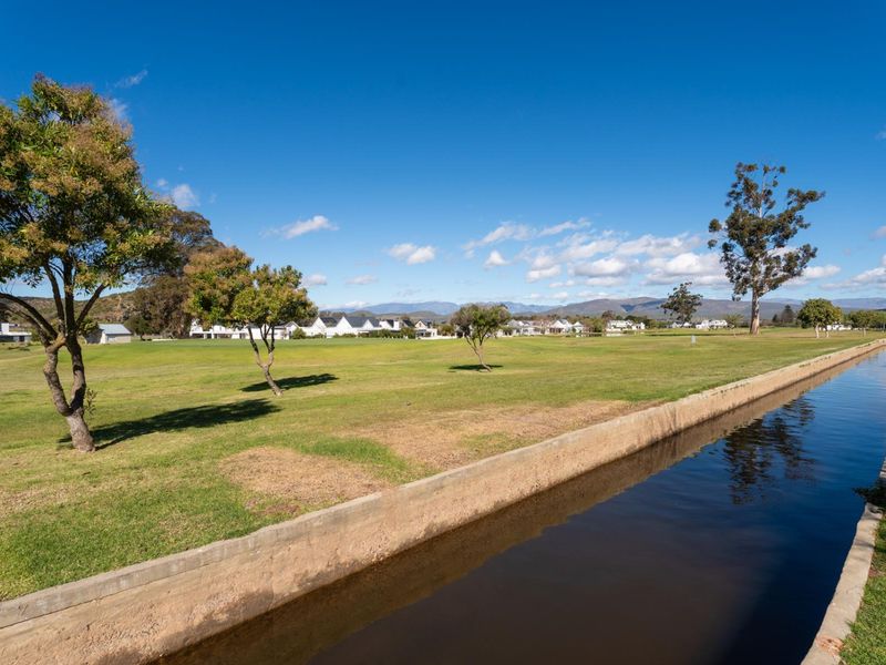 A scenic view of the estate grounds featuring a concrete water channel, expansive manicured lawns, and distant mountain views.
