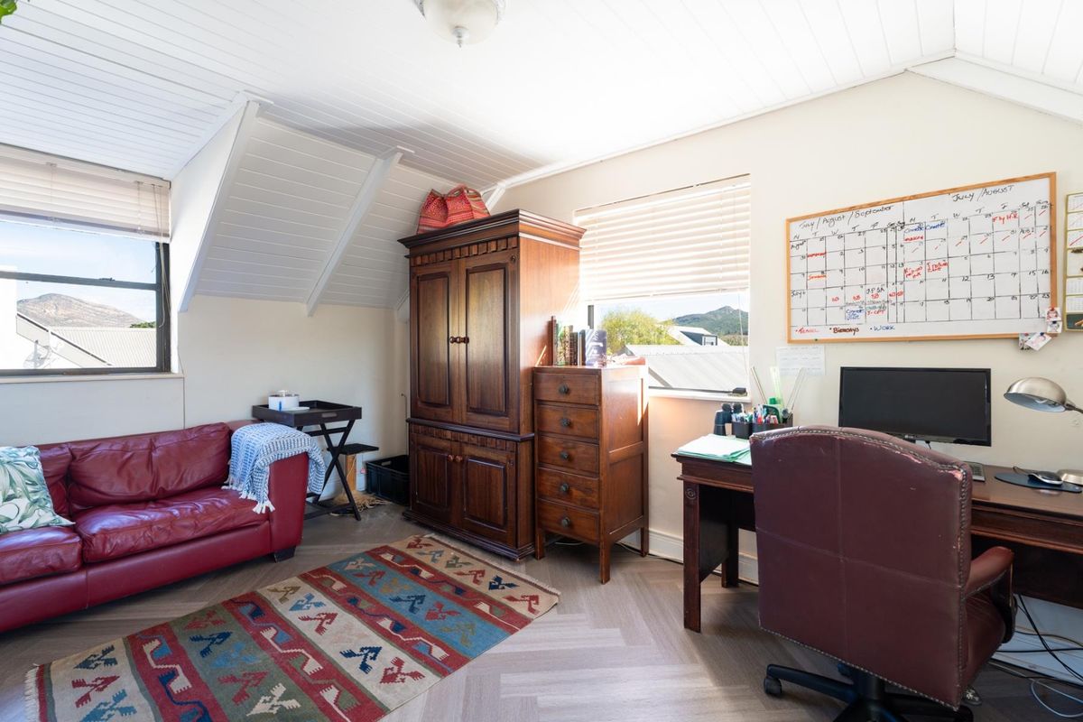 A bedroom featuring sloped ceilings, timber-look vinyl flooring, and natural light through venetian blinds, currently utilized as a home office space.