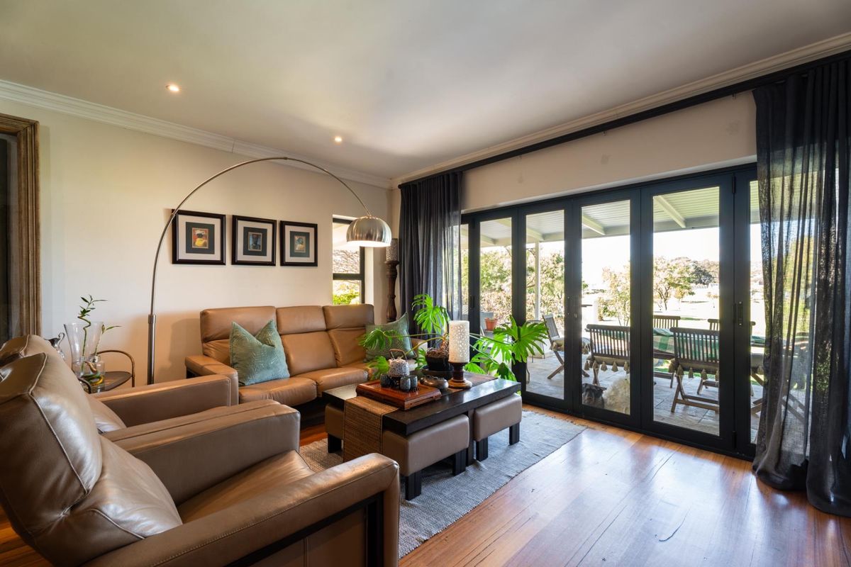 A bright living room featuring polished hardwood flooring, recessed lighting, and large bi-fold glass doors that provide seamless access to the outdoor patio area.