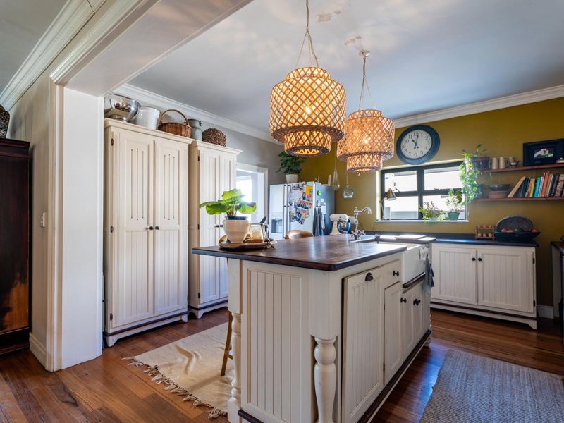 A charming kitchen featuring a central island with a timber countertop, farmhouse sink, and classic white cabinetry set against warm hardwood floors.