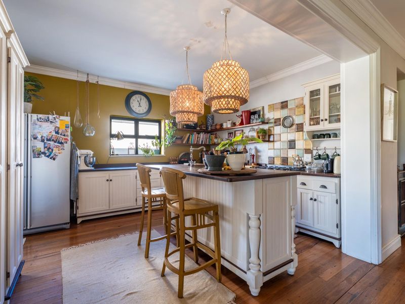A charming kitchen featuring a central island, timber flooring, custom cabinetry, and decorative tiled splashback, creating a warm and functional culinary space.