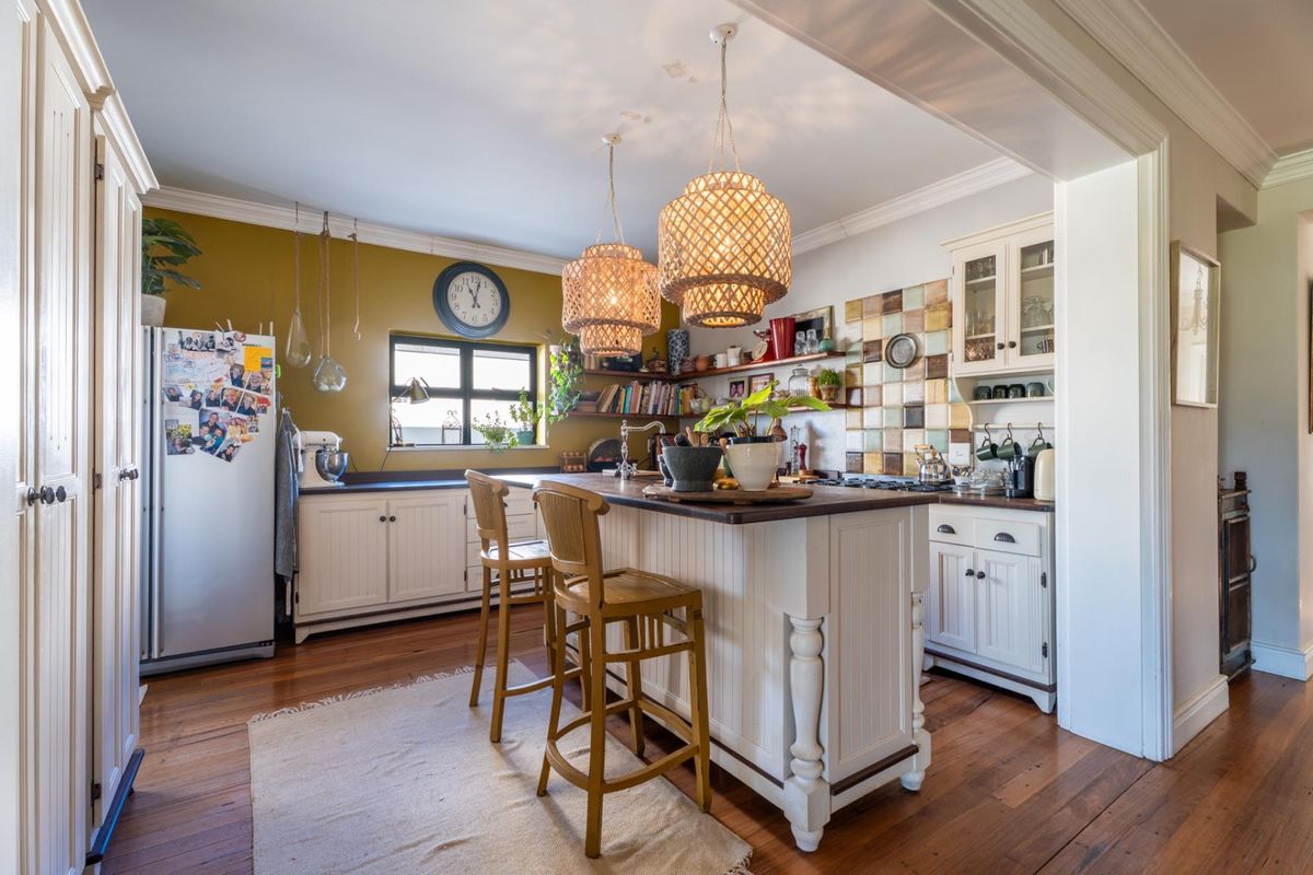 A charming kitchen featuring a central island, timber flooring, custom cabinetry, and decorative tiled splashback, creating a warm and functional culinary space.