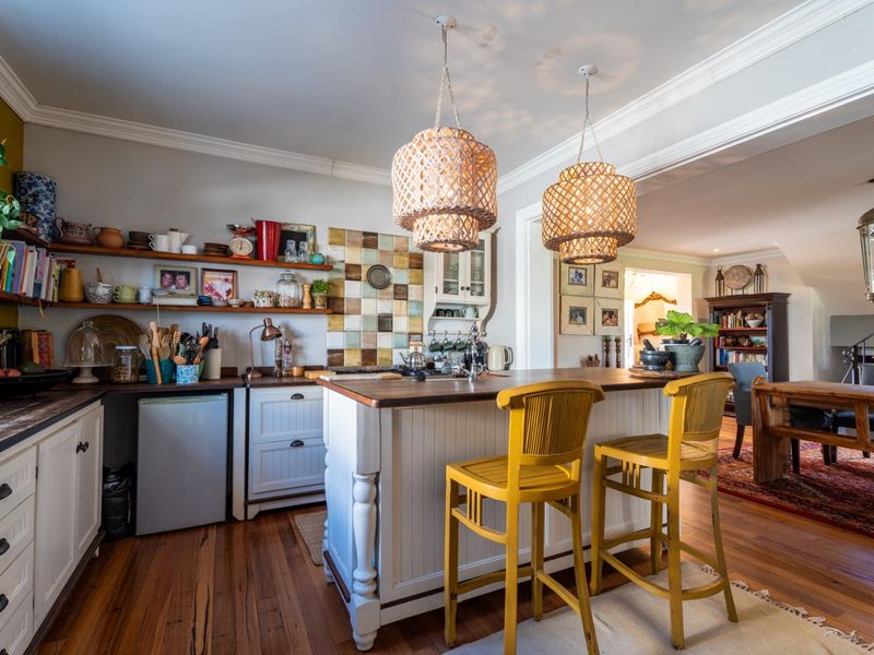 A charming kitchen featuring a central island with timber countertop, tiled splashback, open shelving, and warm timber flooring, seamlessly flowing into the dining area.