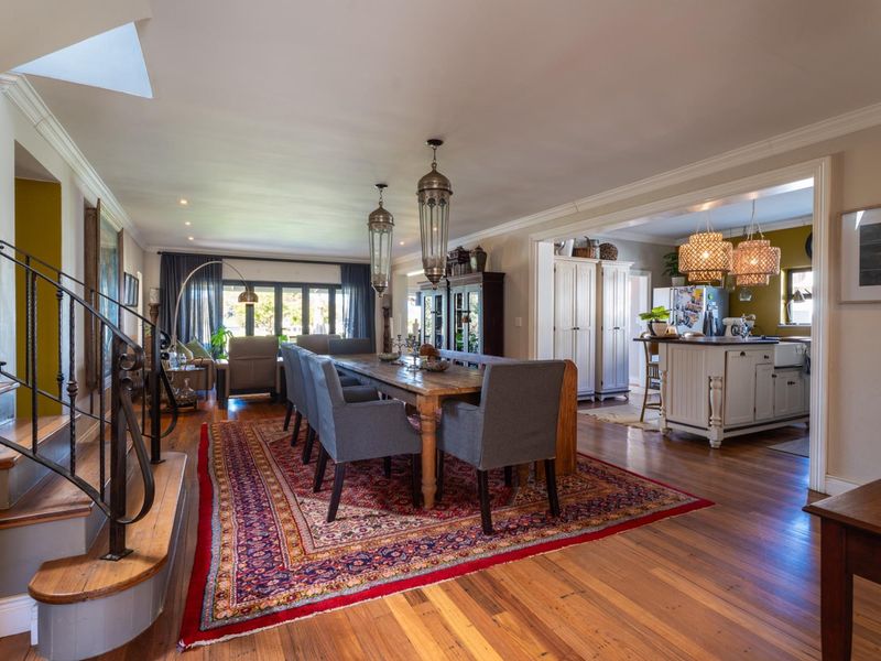 Spacious open-plan dining and kitchen area featuring hardwood flooring, elegant pendant lighting, and a classic staircase with wrought iron railings.