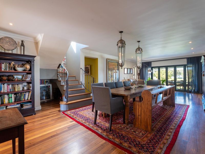Spacious open-plan dining area featuring polished hardwood floors, a feature staircase, and large bi-fold doors providing seamless access to the outdoor patio.