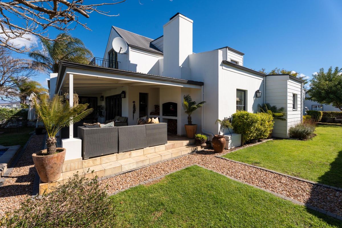 Rear view of the property featuring a covered patio with a built-in braai, overlooking a well-maintained garden and lawn area.