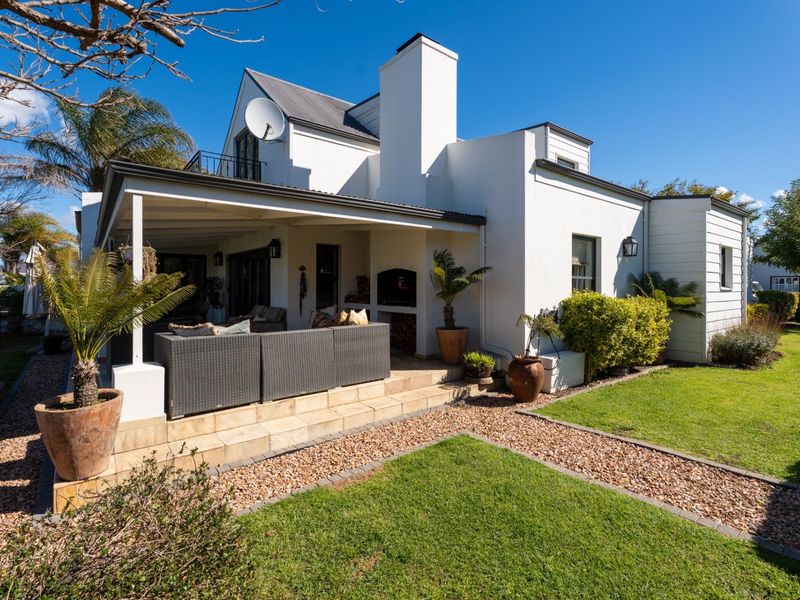 Rear view of the property featuring a covered patio with a built-in braai, overlooking a well-maintained garden and lawn area.