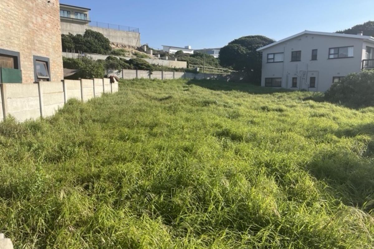 A vacant residential plot featuring a sloped landscape, enclosed by precast concrete boundary walls, situated within an established neighborhood.