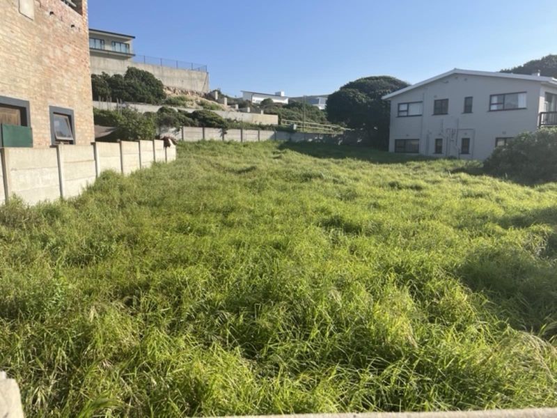 A vacant residential plot featuring a sloped landscape, enclosed by precast concrete boundary walls, situated within an established neighborhood.