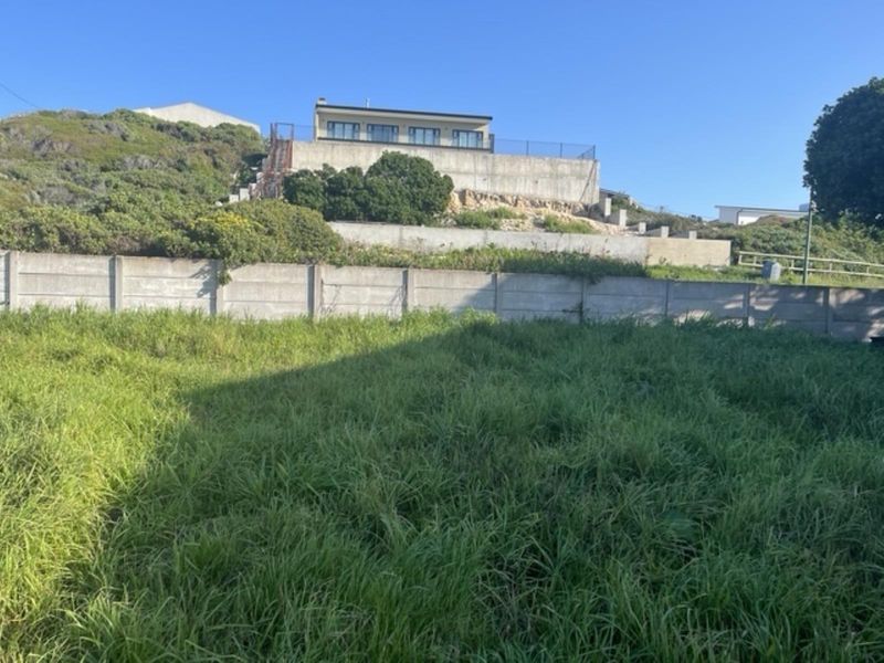 A view of a vacant residential plot featuring a sloped landscape, retaining walls, and a precast concrete boundary wall.