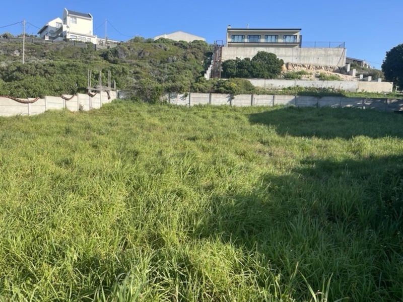 A vacant residential plot featuring a sloped landscape and a precast concrete boundary wall, situated in a developed neighborhood.