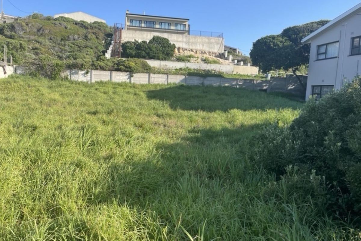 A vacant residential plot featuring sloped terrain, established boundary walls, and a retaining wall, offering potential for development in a residential area.