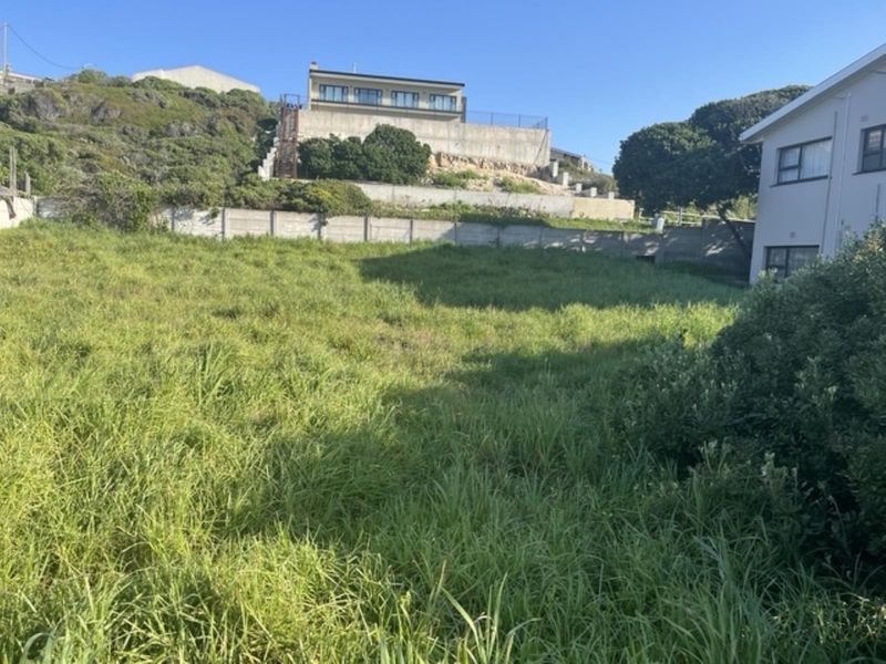 A vacant residential plot featuring sloped terrain, established boundary walls, and a retaining wall, offering potential for development in a residential area.