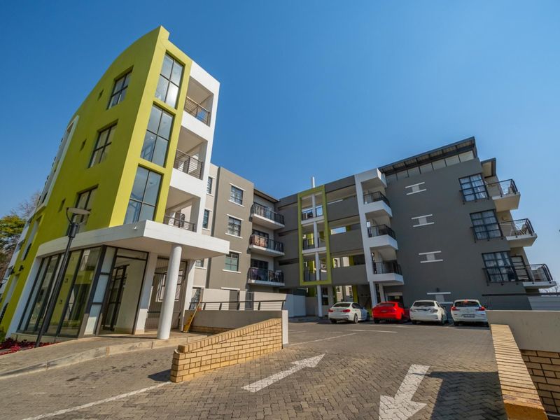 Modern multi-story apartment complex featuring a paved driveway, contemporary facade with lime green accents, and private balconies for each unit.