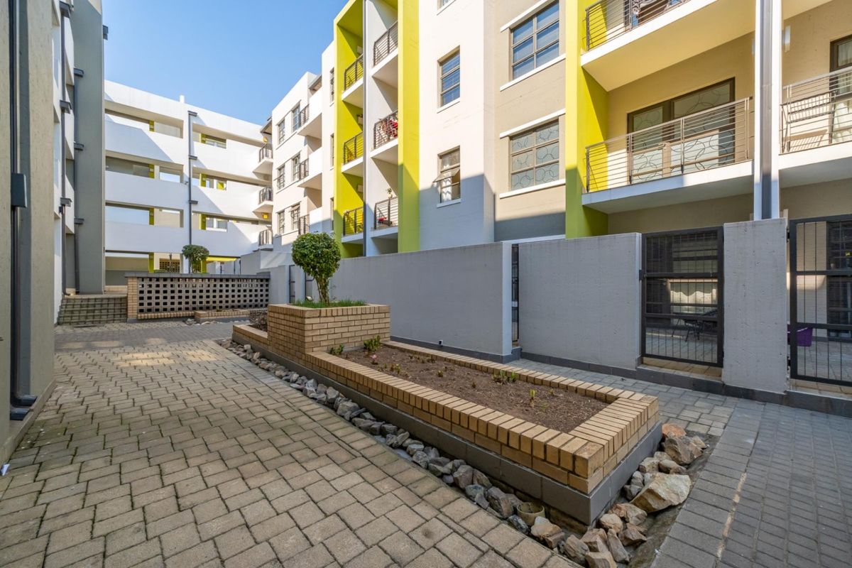 A well-maintained paved courtyard area between apartment blocks featuring a brick planter box and secure metal gate access.