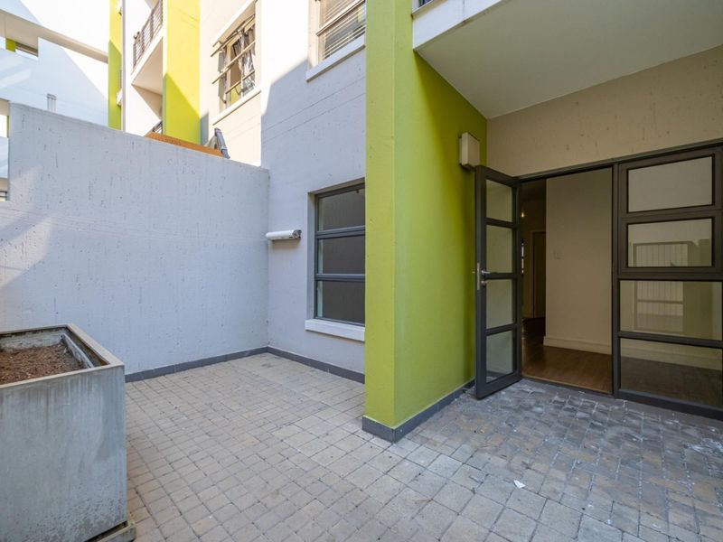 A private paved patio area featuring a built-in planter box and direct access to the apartment interior through a modern glass door.