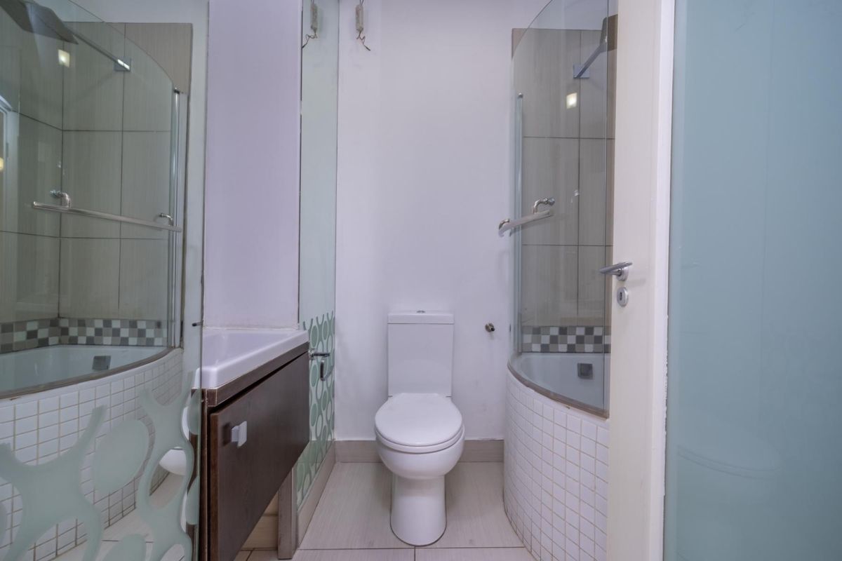 A compact bathroom featuring a toilet, vanity unit, and a glass-enclosed shower with tiled finishes.