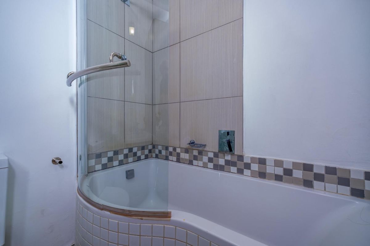 A bathroom featuring a built-in bathtub with a curved glass shower screen, finished with neutral wall tiles and a decorative mosaic border.