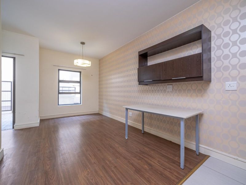 A bright, empty office space featuring laminate flooring, patterned wallpaper, and built-in wall shelving, with access to an outdoor area.