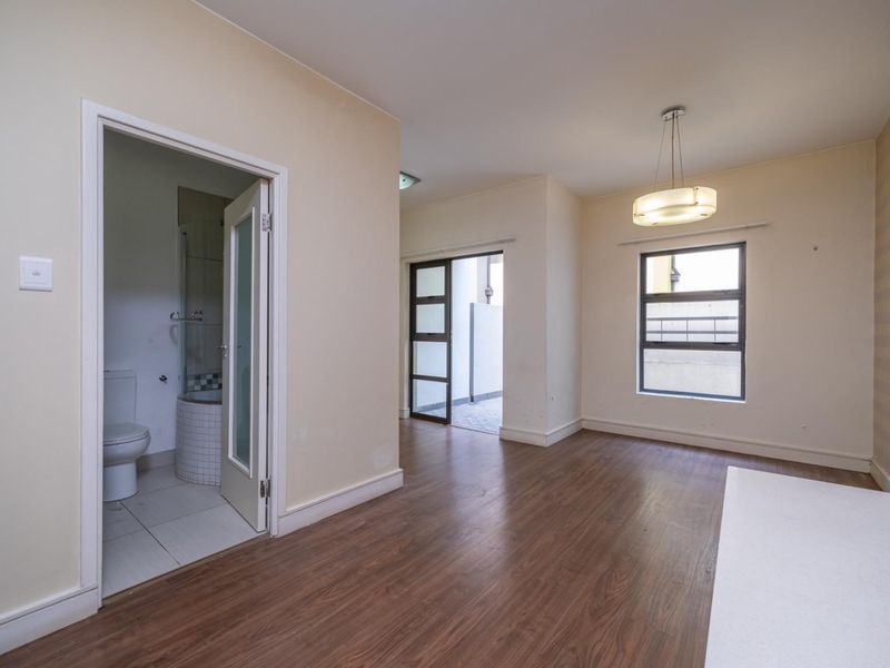 An empty bedroom featuring laminate flooring, an en-suite bathroom, and natural light through aluminium-framed windows.