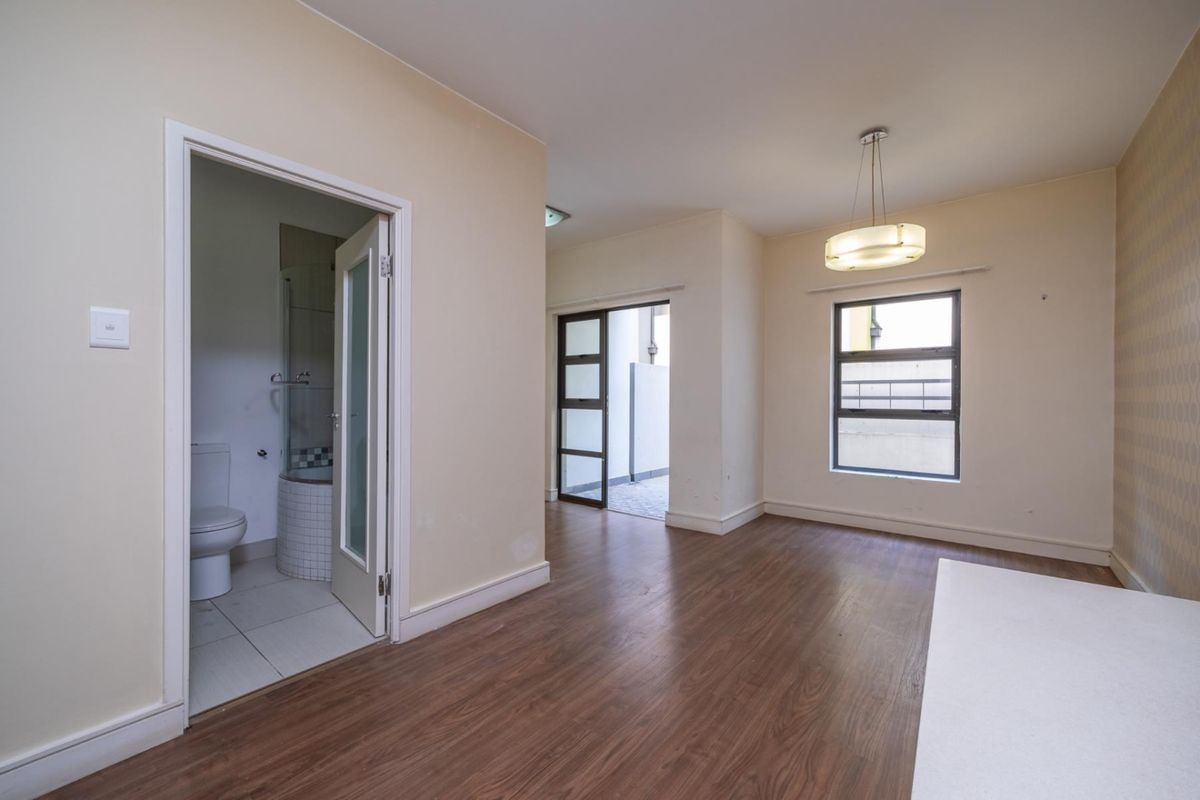An empty bedroom featuring laminate flooring, an en-suite bathroom, and natural light through aluminium-framed windows.
