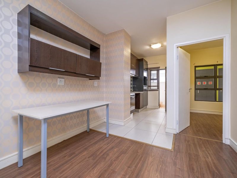 Open plan living area featuring a combination of laminate and tiled flooring, leading into a functional kitchen space with built-in cabinetry and appliances.