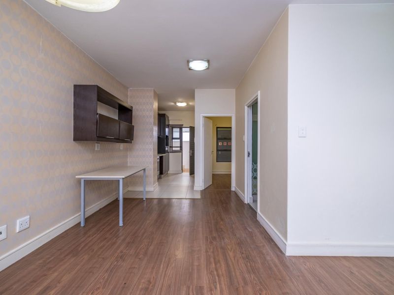 An open-plan living area featuring laminate flooring, built-in wall shelving, and neutral wall finishes, leading through to the kitchen and adjacent rooms.