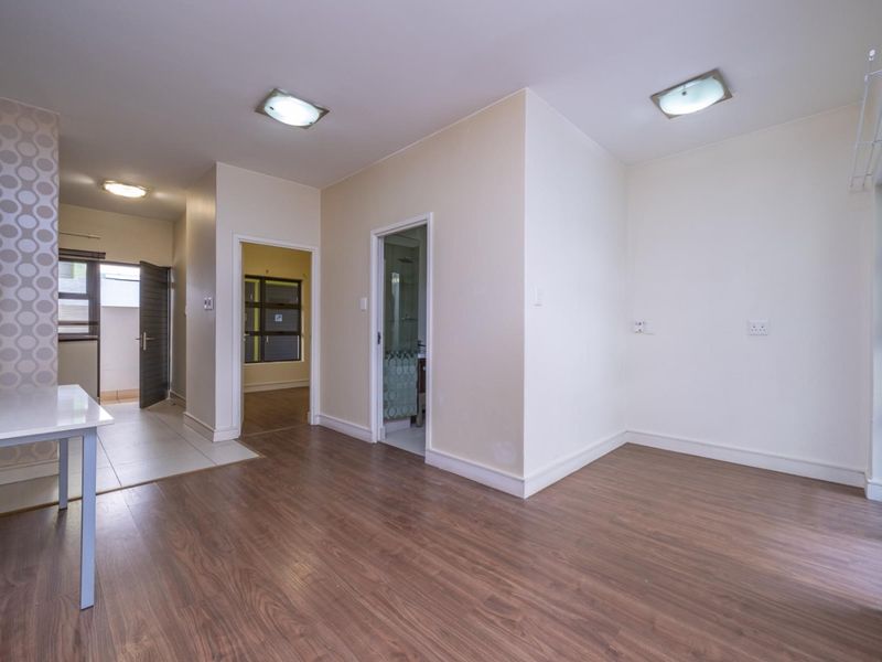 An open-plan living area featuring laminate flooring, neutral walls, and direct access to adjacent rooms, providing a versatile and bright space.