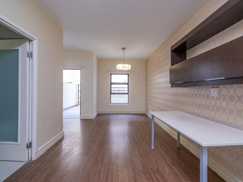 A bright, empty office space featuring laminate flooring, built-in wall shelving, and a fixed desk, offering a versatile area for work or study.