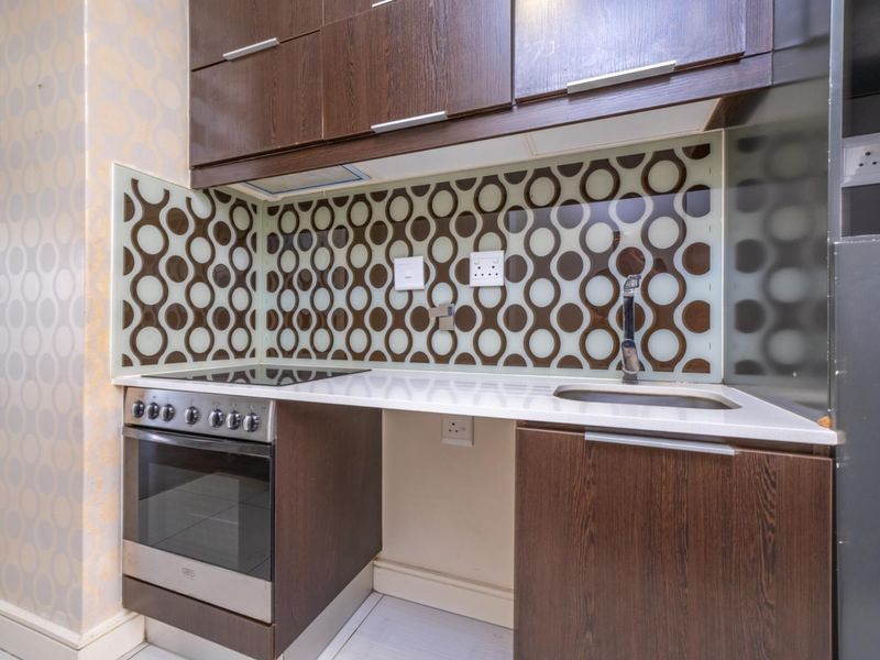 Compact kitchen featuring dark wood cabinetry, a built-in electric stove with oven, stainless steel sink, and a decorative patterned glass splashback.