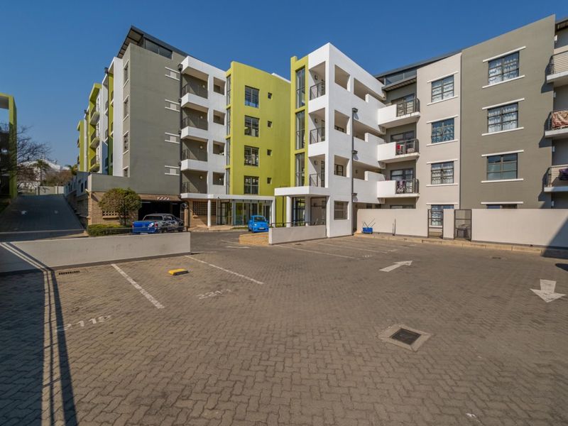 Exterior view of a modern multi-story apartment complex featuring a paved parking area and building facade with balconies.
