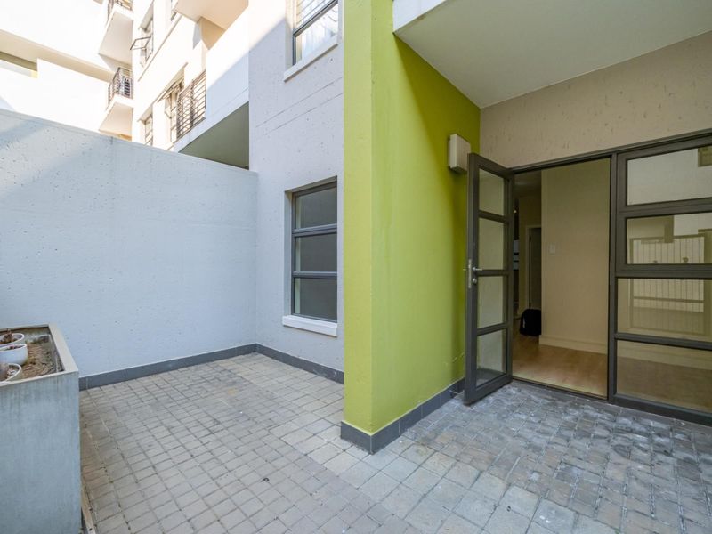 A private ground-floor patio area featuring paved flooring, a built-in planter box, and direct access to the apartment interior through glass-paneled doors.