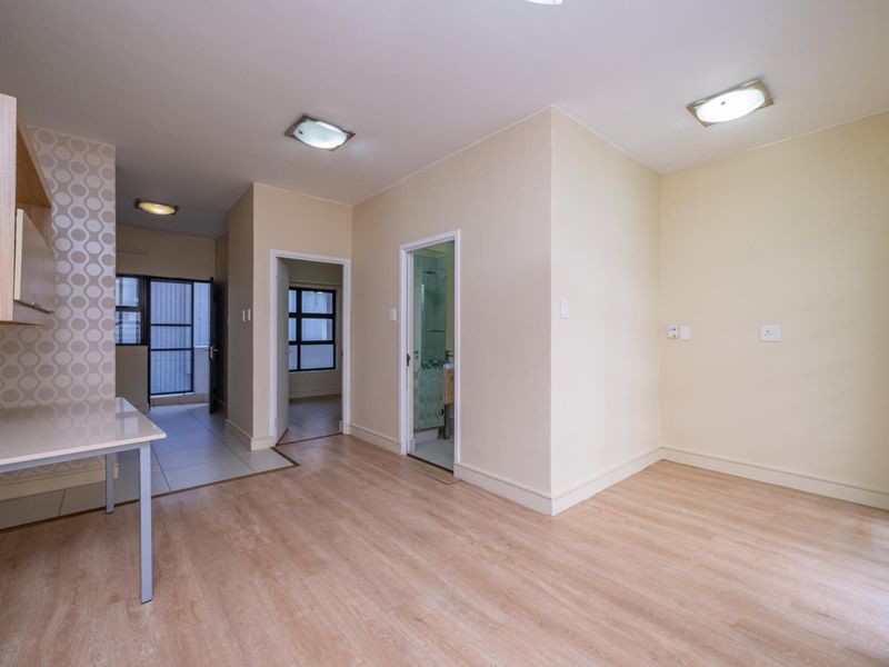 An open-plan living area featuring light laminate flooring, neutral walls, built-in cabinetry, and access to adjacent rooms and a tiled utility space.