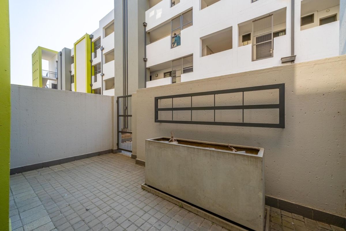 A private paved courtyard area featuring a built-in concrete planter box and secure metal gate access, situated within a modern apartment complex.