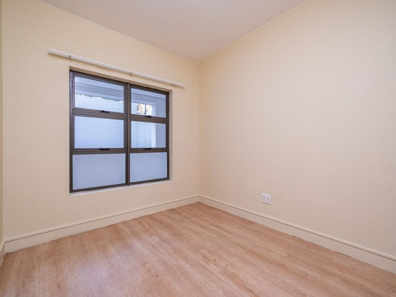 A bright, empty bedroom featuring neutral walls, laminate flooring, and an aluminium-framed window, providing a clean canvas for personalization.