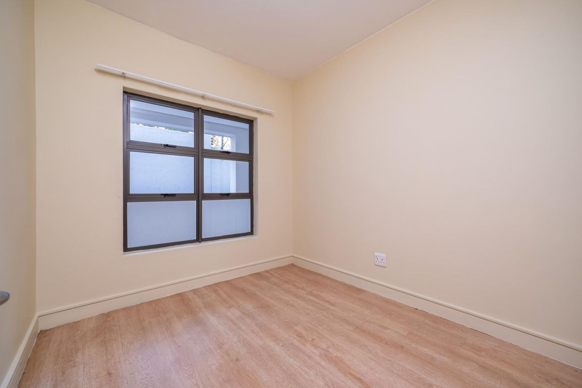 A bright, empty bedroom featuring neutral walls, laminate flooring, and an aluminium-framed window, providing a clean canvas for personalization.