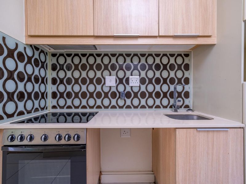 Compact kitchen featuring light wood cabinetry, stone countertops, a modern electric hob with oven, and a decorative patterned glass splashback.