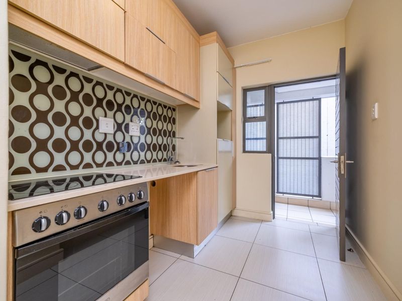 A clean, modern kitchen featuring light wood cabinetry, a built-in oven and hob, patterned splashback, and direct access to an outdoor balcony area.