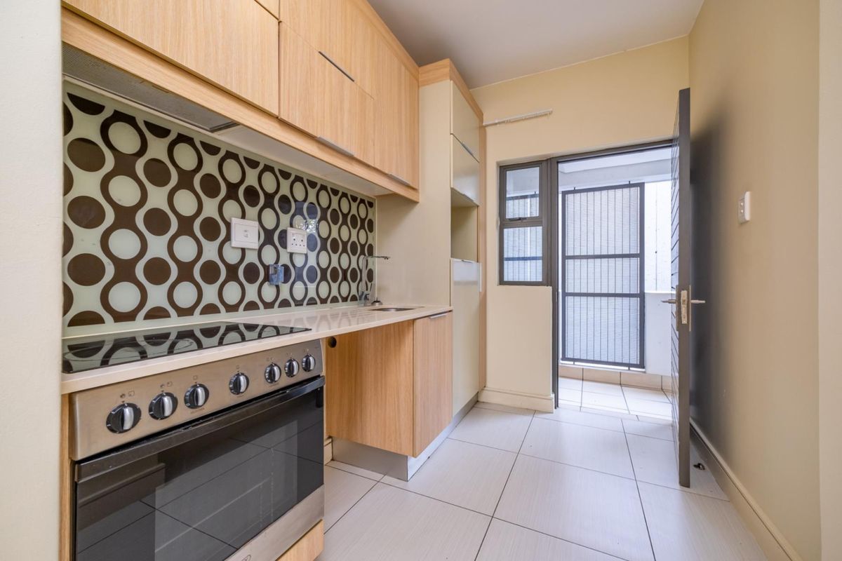 A clean, modern kitchen featuring light wood cabinetry, a built-in oven and hob, patterned splashback, and direct access to an outdoor balcony area.