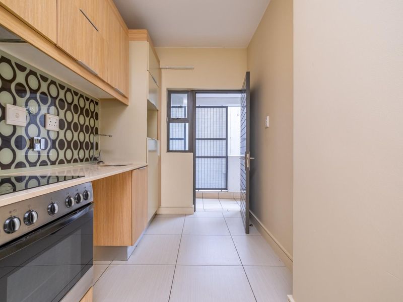 A clean, functional kitchen featuring light wood cabinetry, a modern electric stove, and a distinctive patterned backsplash, leading to an outdoor utility area.