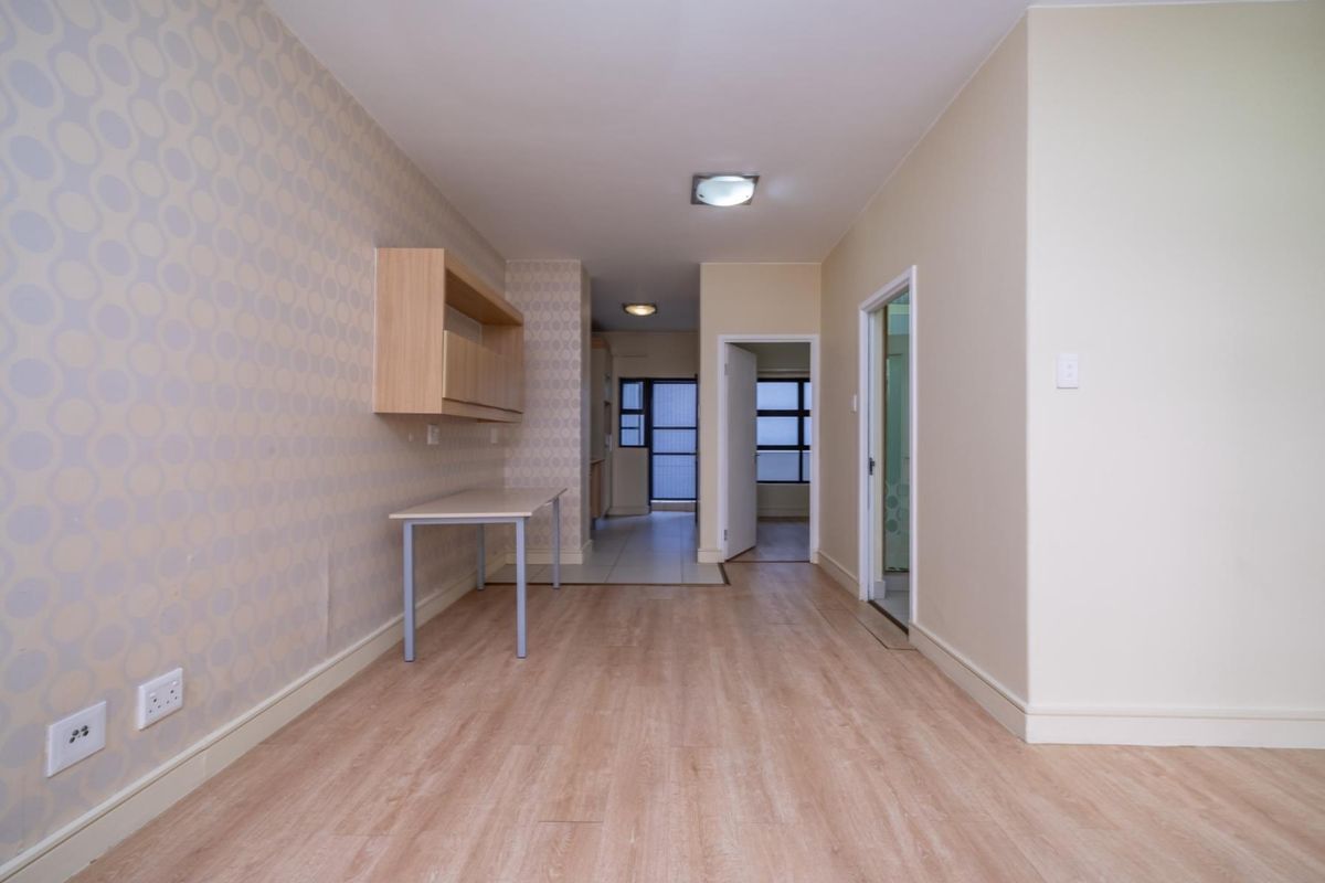 An empty living area featuring light wood-look laminate flooring, patterned wallpaper, and built-in wall shelving, leading through to an adjacent room.