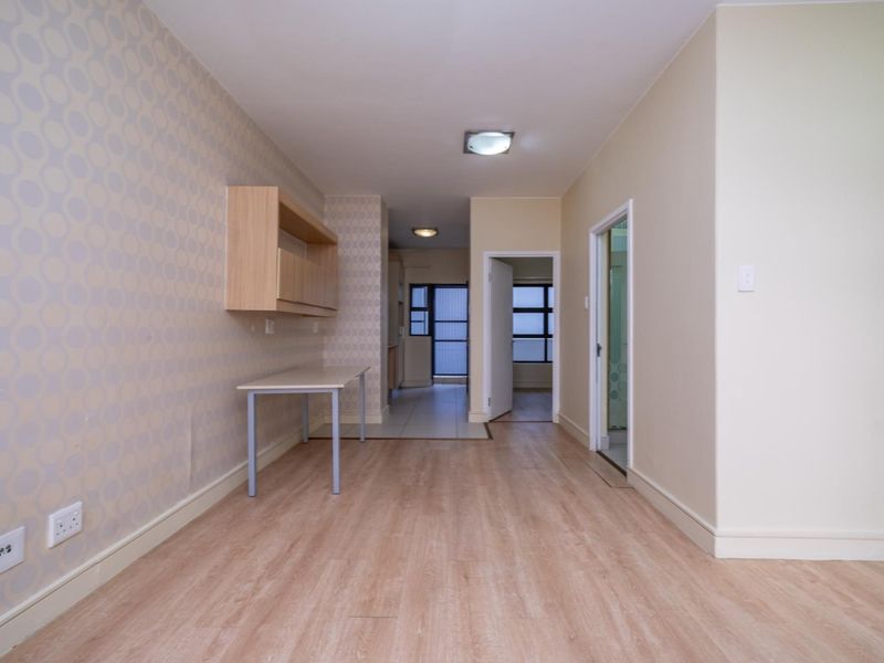 An empty living area featuring light wood-look laminate flooring, patterned wallpaper, and built-in wall shelving, leading through to an adjacent room.