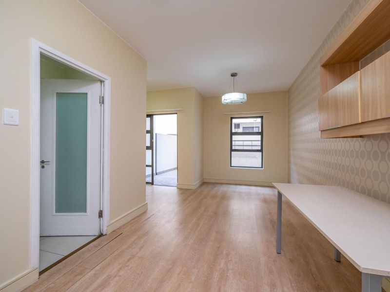 A bright, empty office space featuring laminate flooring, a built-in desk with overhead cabinetry, and a frosted glass door leading to an adjacent area.