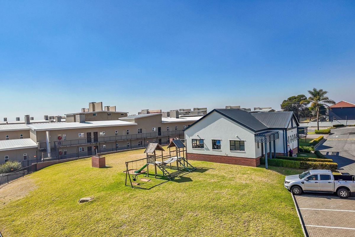 Aerial view of the apartment complex grounds, featuring a communal lawn, playground area, and paved parking facilities.